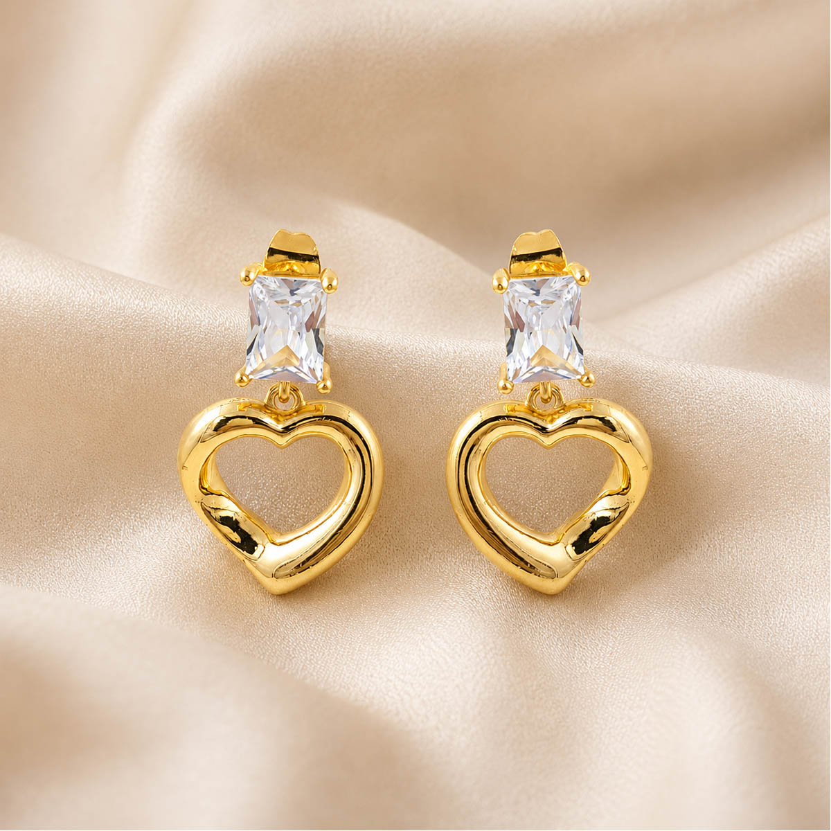 Gold-tone open heart drop earrings with rectangular clear stones on a white background. Gold-tone open heart drop earrings with rectangular clear stones on a white background.